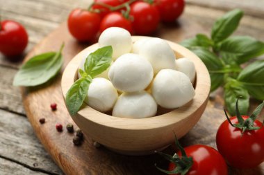 Lezzetli mozzarella peynir topları kasede, fesleğende, biberlikte ve domateslerde ahşap masada, yakın planda.