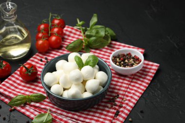 Lezzetli mozarella peynir topları kasede, domates ve baharatlar siyah masada, yakın plan.