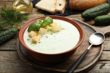 Ahşap masada servis edilen kıtır kıtır salatalık çorbası ve fesleğen.