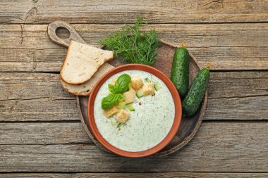 Lezzetli salatalık çorbası, kızarmış ekmek, fesleğen, ekmek ve sebzeler ahşap masada, düzlük.