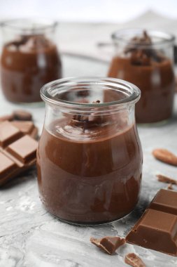 Cam kavanozlarda lezzetli puding ve açık gri masada çikolata parçaları, yakın plan.
