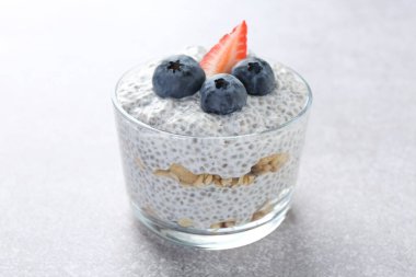 Chia tohumlu lezzetli puding, yoğurt, yaban mersini, granola ve çilek açık gri masada, yakın plan. Süper yemek.