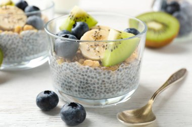 Chia tohumlu lezzetli tatlı, yoğurt, granola, yaban mersini, muz ve kivi beyaz ahşap masada, yakın plan. Süper yemek.