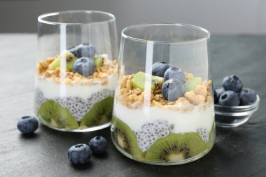 Chia tohumlu lezzetli tatlı, yoğurt, granola, yaban mersini ve kivi gri masada, yakın plan. Süper yemek.