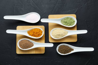 Koyu desenli masada, düz yerde, kaşıklarda farklı süper yiyecek tozları var.