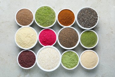 Gri desenli masada, düz yerde, kaselerde farklı süper yiyecek tozları var.