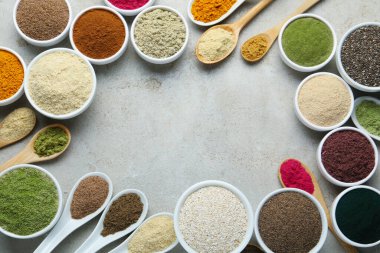 Kâselerdeki farklı süper yiyecek tozlarının çerçevesi ve gri desenli masa üzerindeki kaşıklar düz. Metin için boşluk
