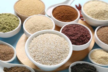 Açık mavi arka planda farklı süper yiyecek tozları, yakın plan