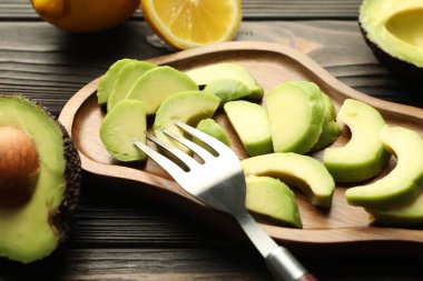 Olgun yeşil avokadolar, ahşap masada limon ve çatal, yakın plan.