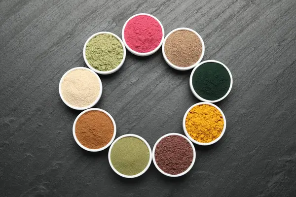 Siyah masa üzerinde farklı süper yiyecek tozları, düz uzanmış.