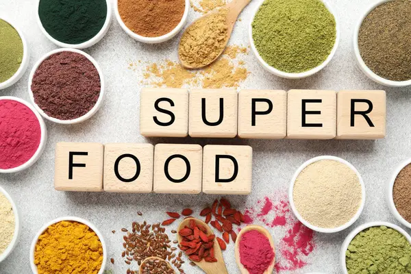 Farklı süper yiyecek tozları ve açık gri masadaki küplerden yapılmış kelimeler.