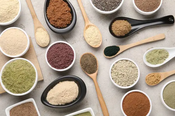 Gri desenli masa üzerinde kaşık ve kâselerde farklı süper yiyecek tozları, düz yatıyordu.