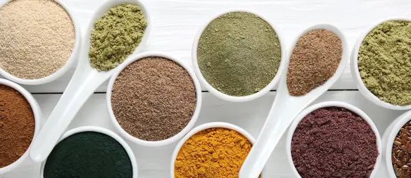 Farklı süper yiyecek tozları kaseler ve kaşıklar beyaz ahşap masa, düz yatıyordu.