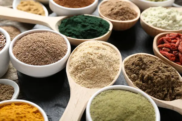 Kaşık ve kaselerdeki farklı süper yiyecekler siyah masada, yakın plan.