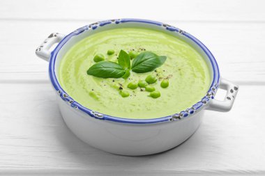 Beyaz ahşap masada fesleğenli bezelye kremalı çorba, yakın plan.