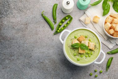 Gri masada servis edilen kızarmış ekmek ve fesleğenli bezelye kremalı çorba. Metin için boşluk