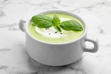 Fesleğenli bezelye kremalı çorba beyaz mermer masada servis edilir, yakın plan.