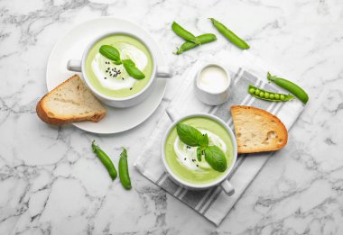 Fesleğenli bezelye kremalı çorba beyaz mermer masada servis edilir, düz yatar.