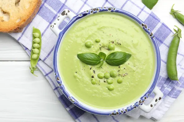 Beyaz ahşap masada servis edilen fesleğenli bezelye kremalı çorba.