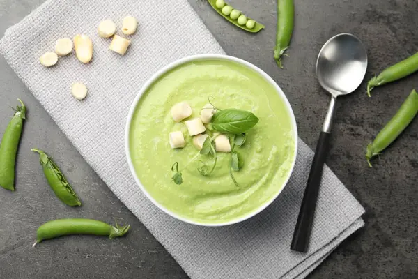 Lezzetli bezelye kremalı çorba, kızarmış ekmek, fesleğen ve mikroyeşillikler gri masada servis edilir.