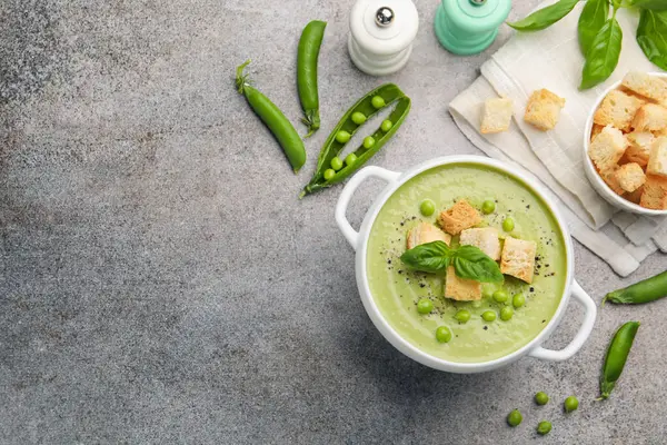 Gri masada servis edilen kızarmış ekmek ve fesleğenli bezelye kremalı çorba. Metin için boşluk