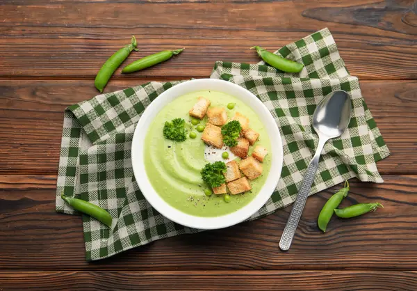 Tahta masada servis edilen kızarmış ekmek ve brokoli ile bezelye kremalı leziz çorba.