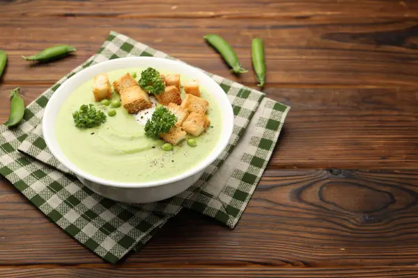 Ahşap masada servis edilen kızarmış ekmek ve brokolili bezelye kremalı çorba. Metin için boşluk