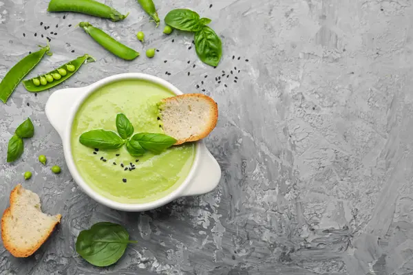 Lezzetli bezelye kremalı çorba, fesleğen ve kızarmış ekmek, gri masada servis edilir. Metin için boşluk