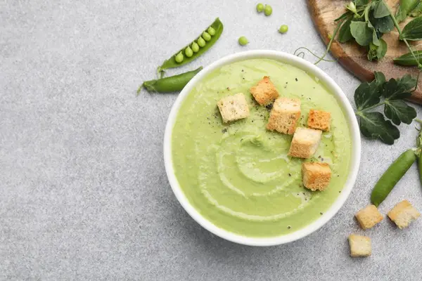 Gri masada servis edilen kıtır ekmekli bezelye kremalı çorba.