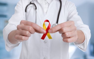 Dünya Hepatit Günü. Bulanık arka planda sarı-kırmızı farkındalık kurdelesi olan doktor, yakın plan.