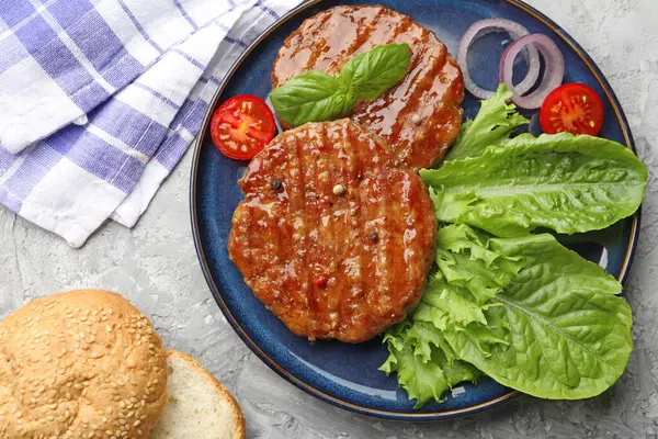 Lezzetli hamburger köfteleri, domates, marul, çörekler ve baharatlar gri masada, düz konum