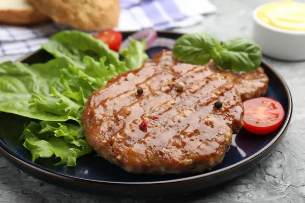 Lezzetli hamburger köfteleri, domates, marul ve baharatlar gri masada, yakın plan.