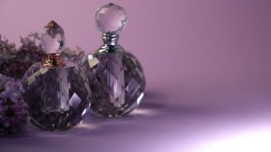 Parfüm şişeleri ve mor arka planda güzel leylak çiçekleri, metin için yer. Işığın yönü değiştiriliyor