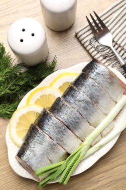 Limon dilimli lezzetli ringa balıkları, yeşil soğan ve ahşap masa üzerinde dereotlar.