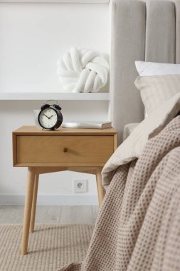 Alarmlı komodinli komodin, bir bardak su ve yatağın yanında kitap.