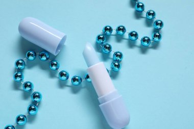 Nemlendirici dudak kremi ve açık mavi arka planda Noel dekoru, düz yatış. Kış bakımı