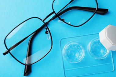 Açık mavi zemin üzerinde kontak lensler ve gözlükler, düz yatar