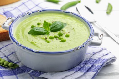 Beyaz ahşap masada servis edilen fesleğenli bezelye kremalı çorba.