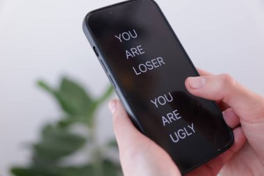 Siber zorbalık. Bulanık arkaplanda akıllı telefon tutan kadın, yakın plan.