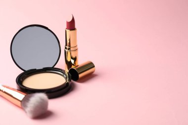 Aynalı açık yüz pudrası, pembe arka planda ruj ve fırça, yakın plan. Metin için boşluk