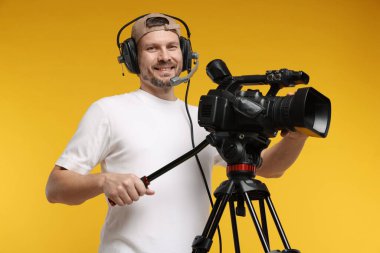 Profesyonel kamera ve turuncu arka planda kulaklığı olan bir adam.