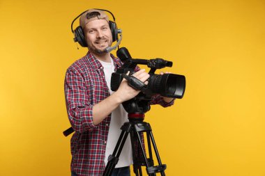 Profesyonel kamera ve turuncu arka planda kulaklığı olan bir adam.