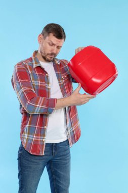 Açık mavi arka planda plastik kutu tutan adam.