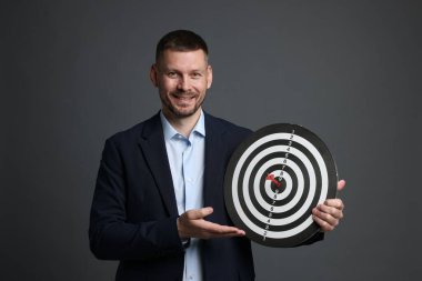 Hedef alınıyor. Dart tahtası ve gri arka planda oku olan bir adam.