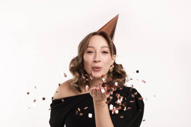 Doğum günü kutlaması. Parti konisi olan bir kadın beyaz arka planda konfeti üflüyor.