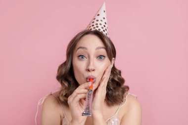 Doğum günü kutlaması. Pembe arka planda parti kornası çalan kadın.