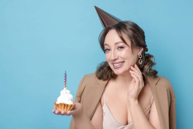 Doğum günü kutlaması. Açık mavi arka planda kek yiyen kadın.