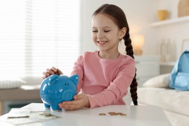 Kız cep harçlığını kapalı bir masadaki domuz kumbarasına yatırıyor.