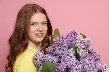 Pembe arka planda leylak çiçekleri olan gülümseyen genç kız portresi