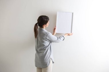 Beyaz duvarda boş bir çerçeve asılı kadın, arka manzara